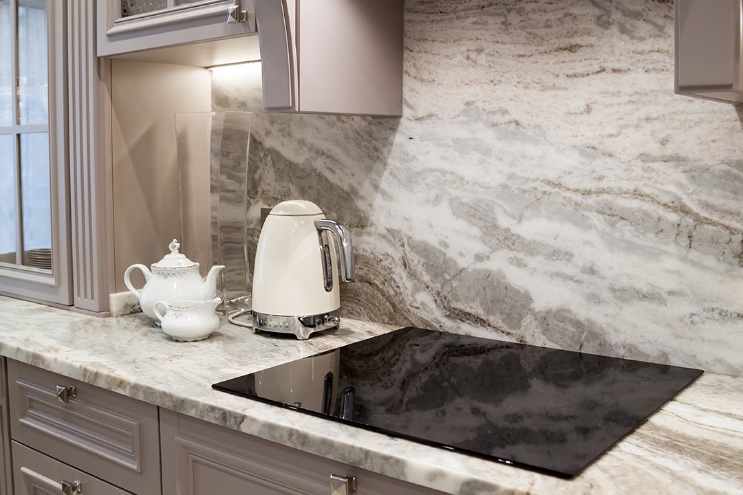 A modern kitchen countertop with a black induction cooktop, white kettle and teapot.