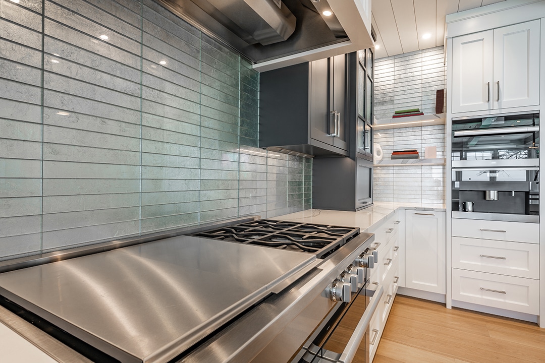 Stainless steel stove in modern kitchen. White cabinets and backsplash.