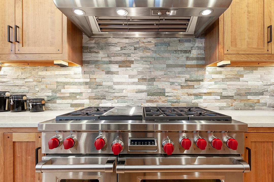 Modern kitchen stove with red knobs. Stainless steel finish.