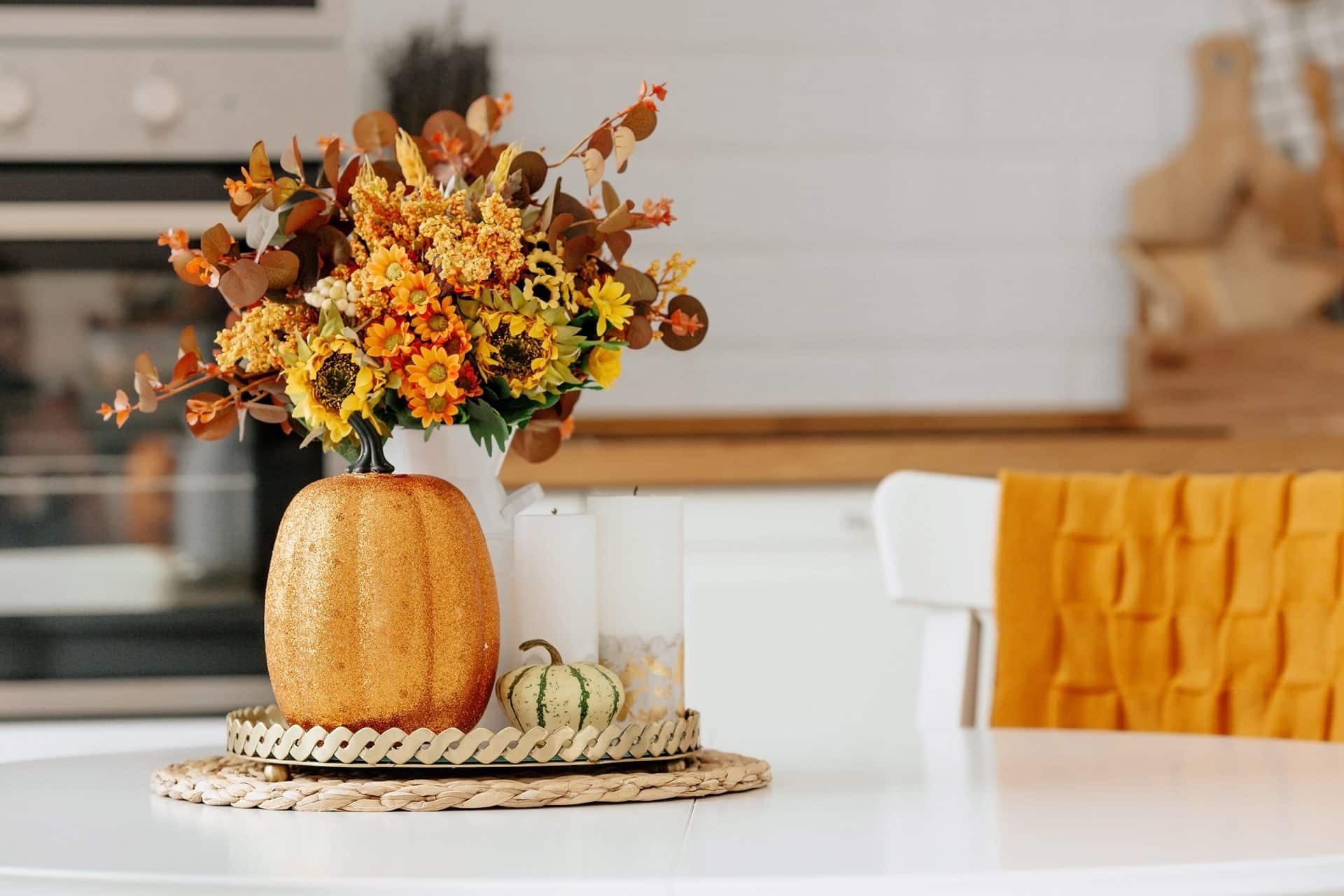 A decorative pumpkin with flowers and small gourds on a table. The arrangement is placed on a woven mat.