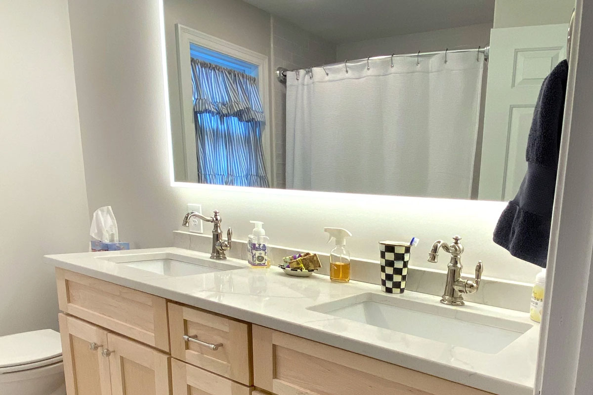 A modern bathroom with a double sink vanity and a large mirror. The vanity has two sinks, two faucets, and a white countertop.