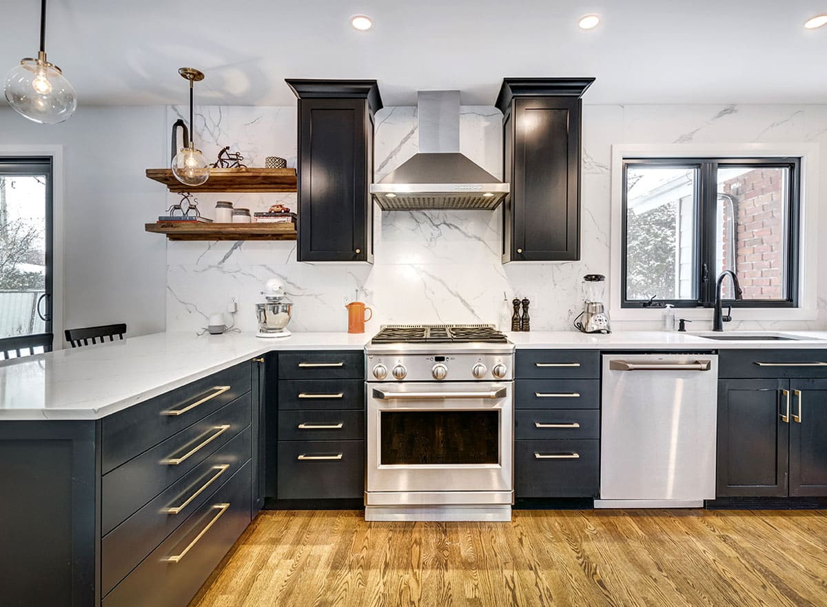 A sleek kitchen with black cabinets, white marble backsplash, and stainless steel appliances. The room is well-lit with natural light.