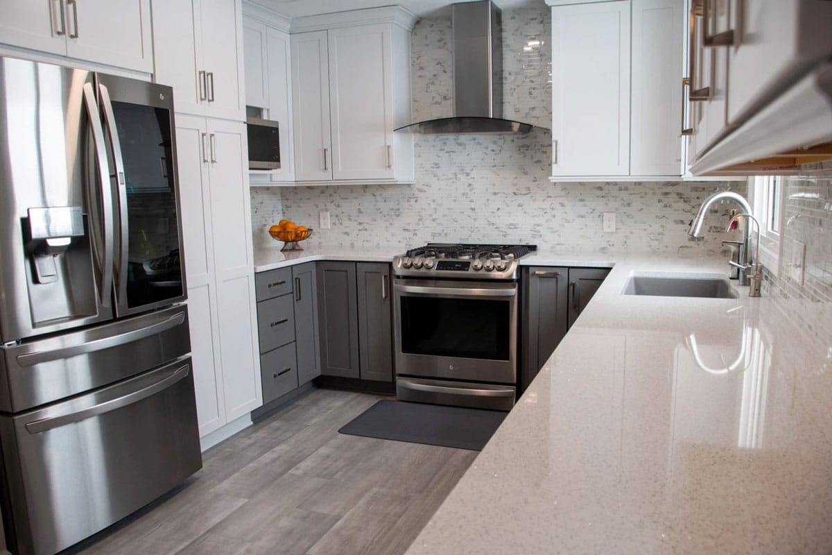 Modern kitchen with stainless steel appliances and white countertops. Gray and white cabinets.