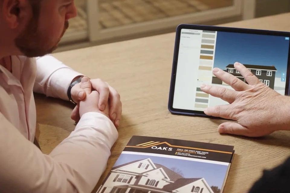 Man and woman looking at tablet with house design and brochure on table