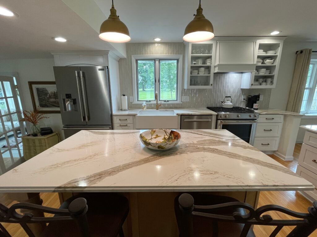 Kitchen island with marble countertop and bowl of fruit. Modern kitchen with white cabinets and stainless steel appliances.