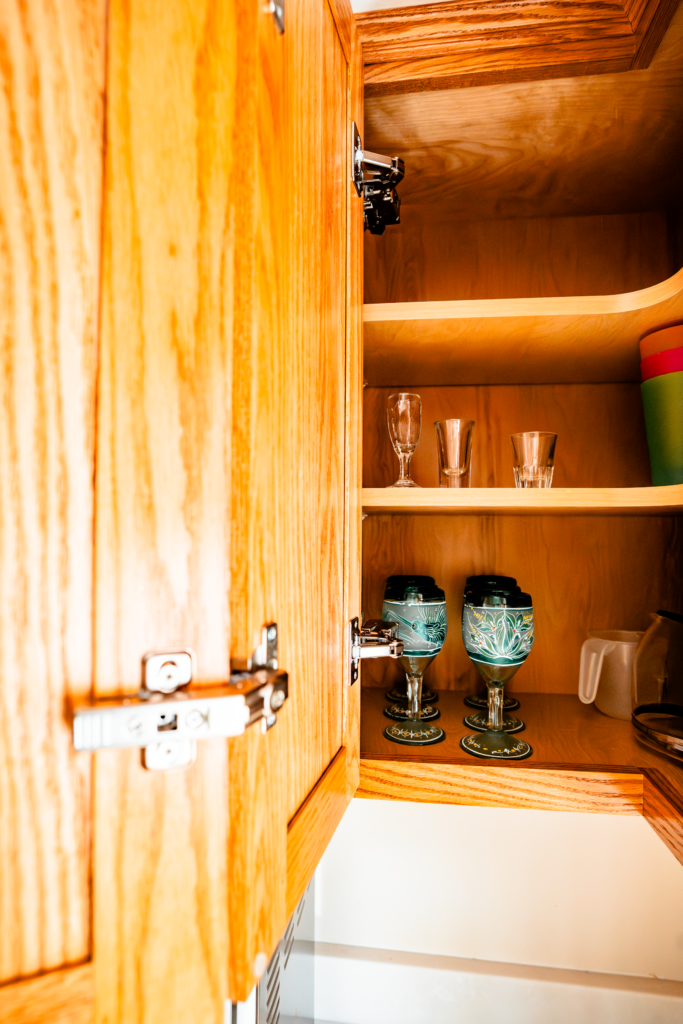 A wooden cabinet with glasses and dishes. The cabinet is open.