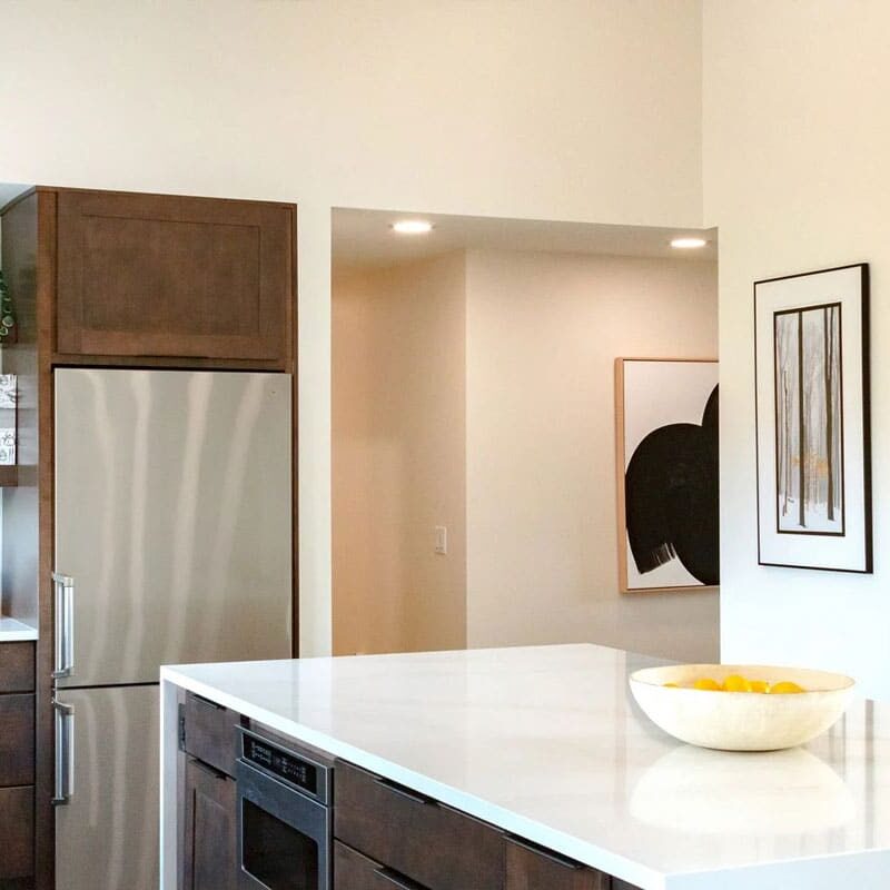 Modern kitchen with white countertop and stainless steel fridge. Kitchen island with bowl of fruit.