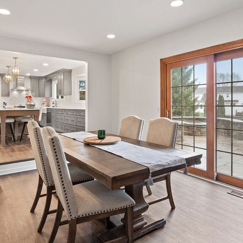 A dining room with a wooden table and chairs. The room has a sliding glass door leading to a patio.