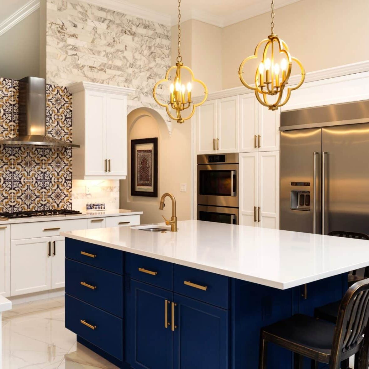 A modern kitchen with a large white island and blue base. The kitchen features stainless steel appliances and white cabinets.