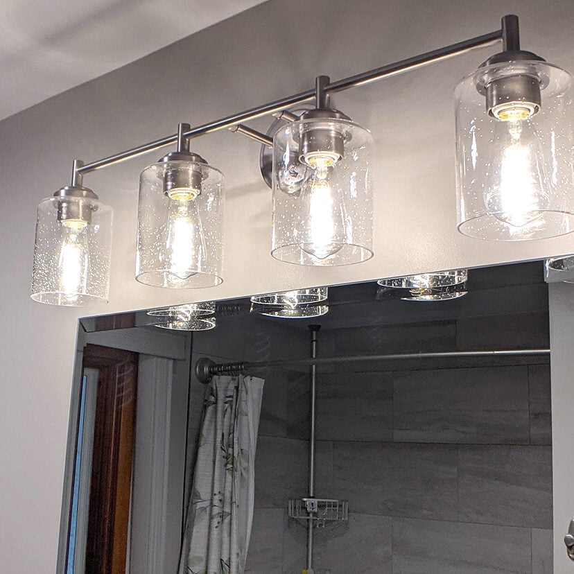 Light fixture with glass shades above a bathroom mirror. Illuminated bulbs inside.